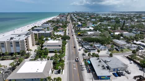 straight street along sandy beach of indian rocks, florida. palm trees, apartment blocks in first row and clear water of gulf sea. aerial wide shot.