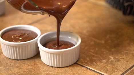 pouring individual homemade portions of chocolate pot de crème into individual serving cups - slow motion