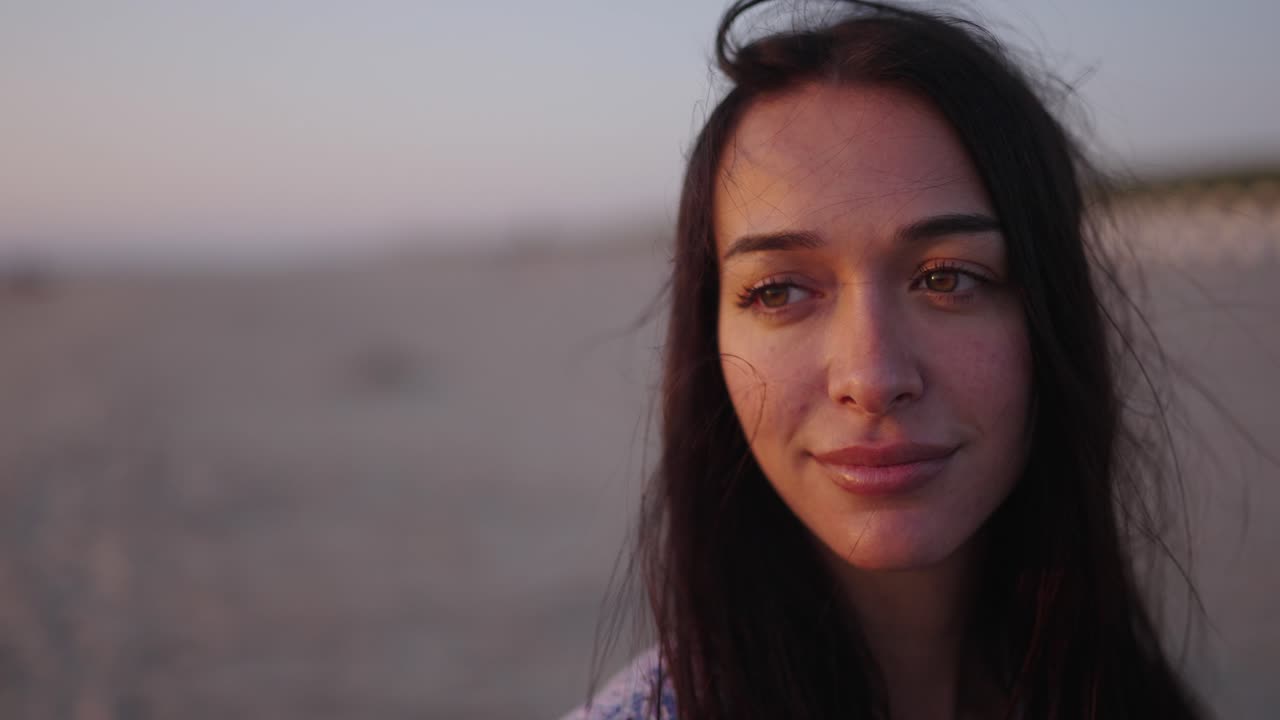 Closeup on pretty brunette's face with loose hair in sea breeze, content smile with closed eyes to savor moment