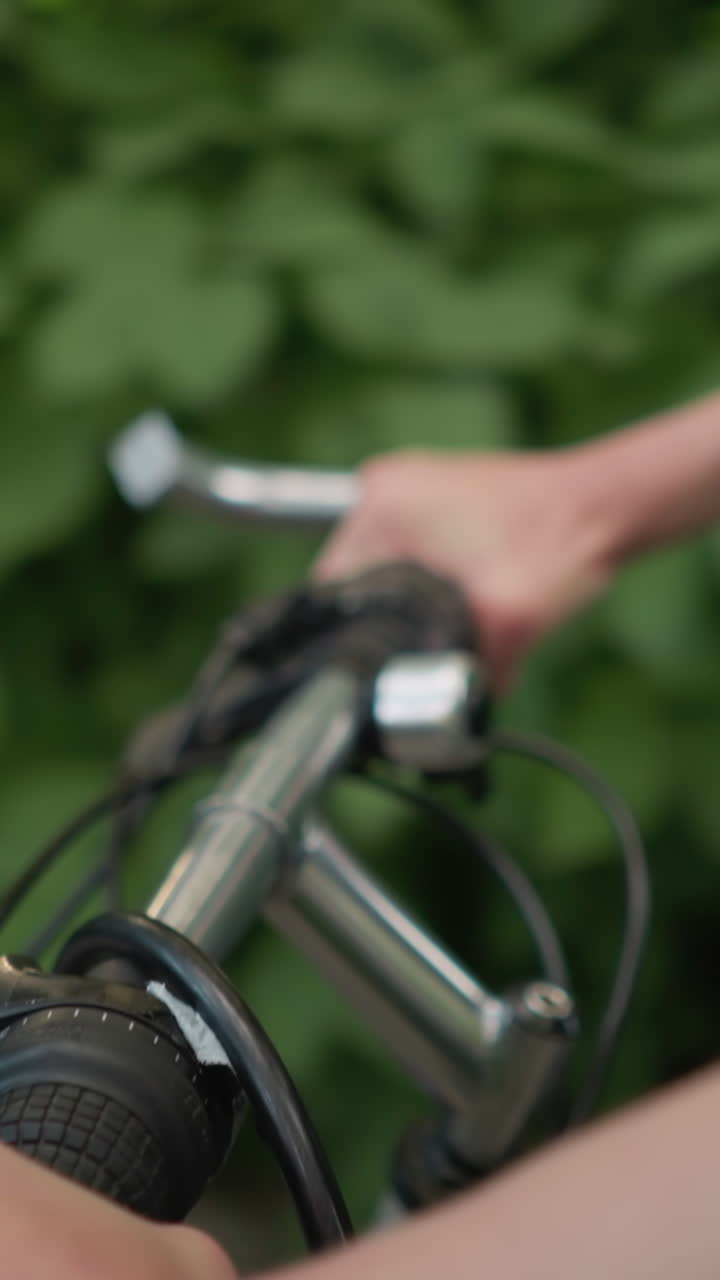 primer plano de la mano del ciclista sosteniendo el manillar, montando a lo largo de un camino pavimentado rodeado de exuberante vegetación, la luz se refleja en el brazo del ciclista mientras avanza con un efecto de fondo bokeh