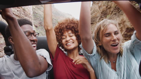 group of young friends in back of open top hire car on summer vacation