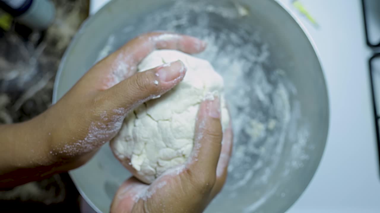 close up view of African american woman's hands kneading pizza dough in a silver pan in slow motion