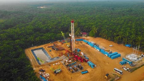 toma cinematográfica de drones de perforación en tierra y estructura de plataforma de reacondicionamiento y equipo de plataforma para exploración y explotación de petróleo en medio de la jungla rodeada de palmeras durante la puesta de sol
