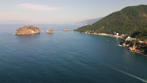 ocean ripples spread across open blue waters as boat exits calm serene bay, drone