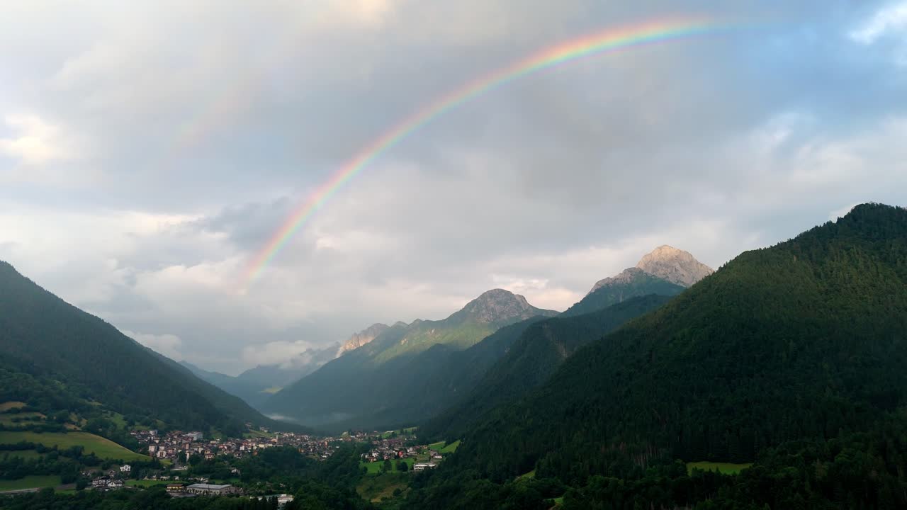 Aerial drone view of a fairytale landscape in Val di Scalve, Italian Dolomites and Alpi Orobie, featuring a vibrant rainbow arching over lush alpine valleys and mountain peaks