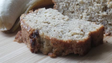una rebanada recién horneada de pan de plátano sentada en una tabla de cortar de madera a la luz natural, de cerca