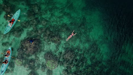 aerial shot of a girl floating on seawater with people kayaking around