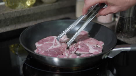 Man-Frying-Pork-Slices-in-a-Pan-At-Home-Kitchen,-Pork-Chop-loins-Being-Turned-Over-With-Tongs