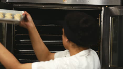 Mujer-En-La-Panadería-Colocando-Bandejas-De-Galletas-En-Un-Horno-Para-Hornear.