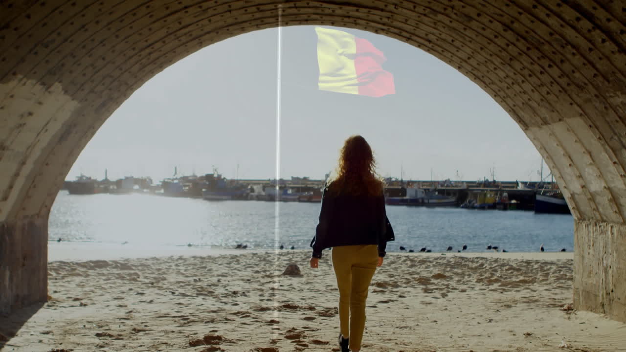Woman walking on sandy beach under arch with flag animation above