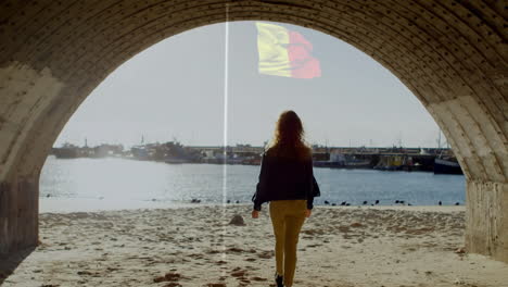 woman walking on sandy beach under arch with flag animation above