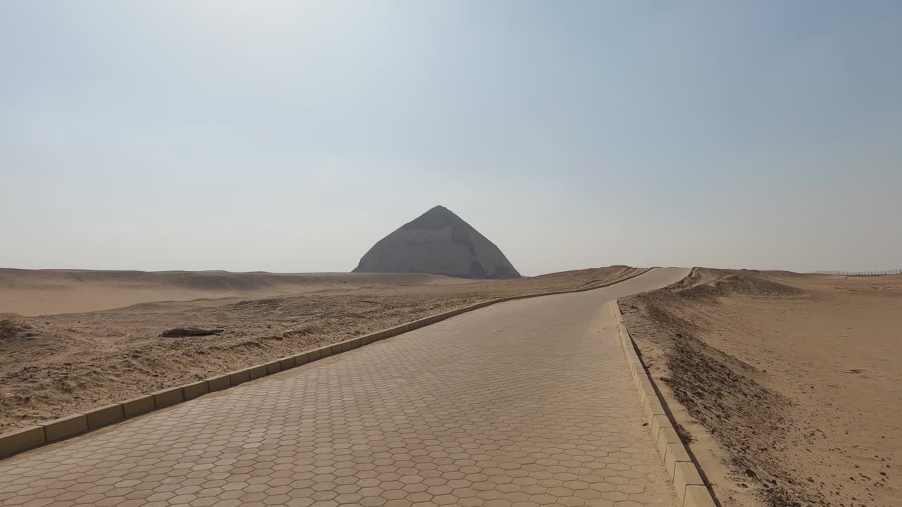 먼 거리에서 구부러진 피라미드까지 사막의 돌길에서 볼 수 있습니다.