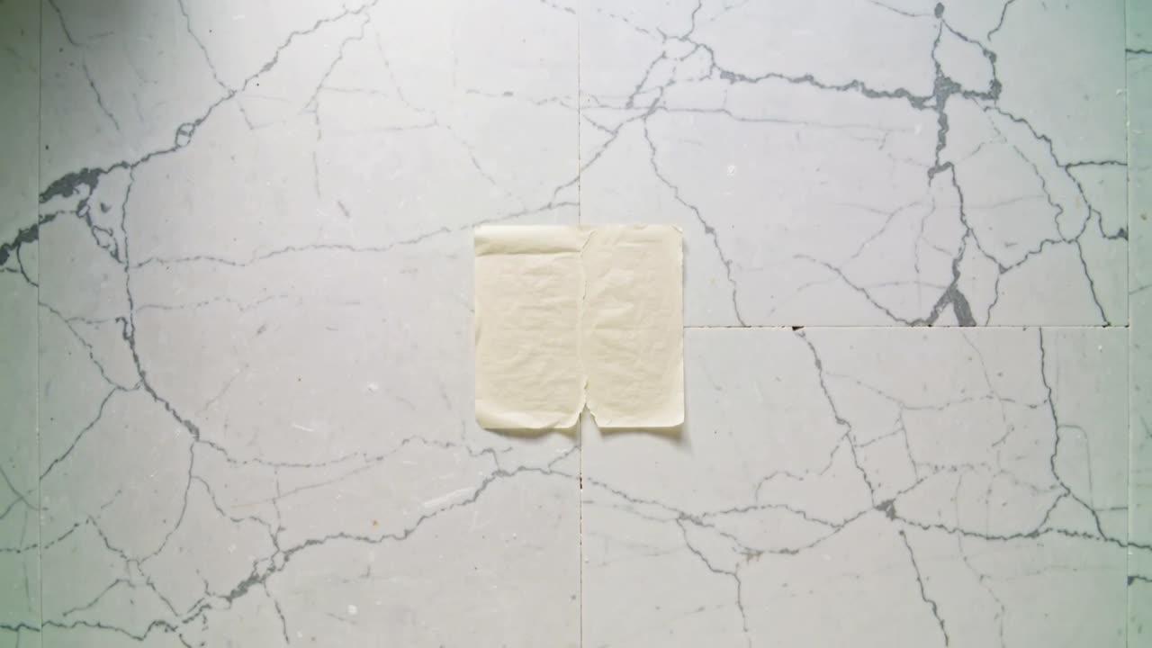 Un piccolo quadratino di pasticcino rimane appoggiato su una piastrella di marmo mentre la telecamera si sposta, rivelando una cucitura a V.