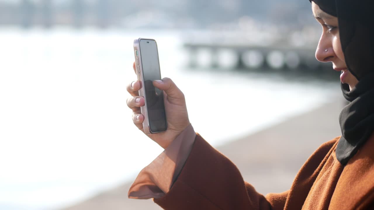 mujer sonriente en un hijab usando un teléfono