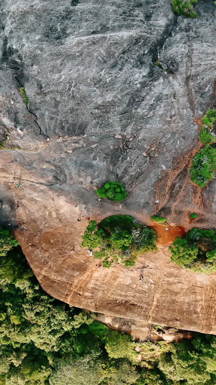 Panning footage above the bare rock. Tourists walk by the mountain top. Sri Lanka from top. Vertical video.