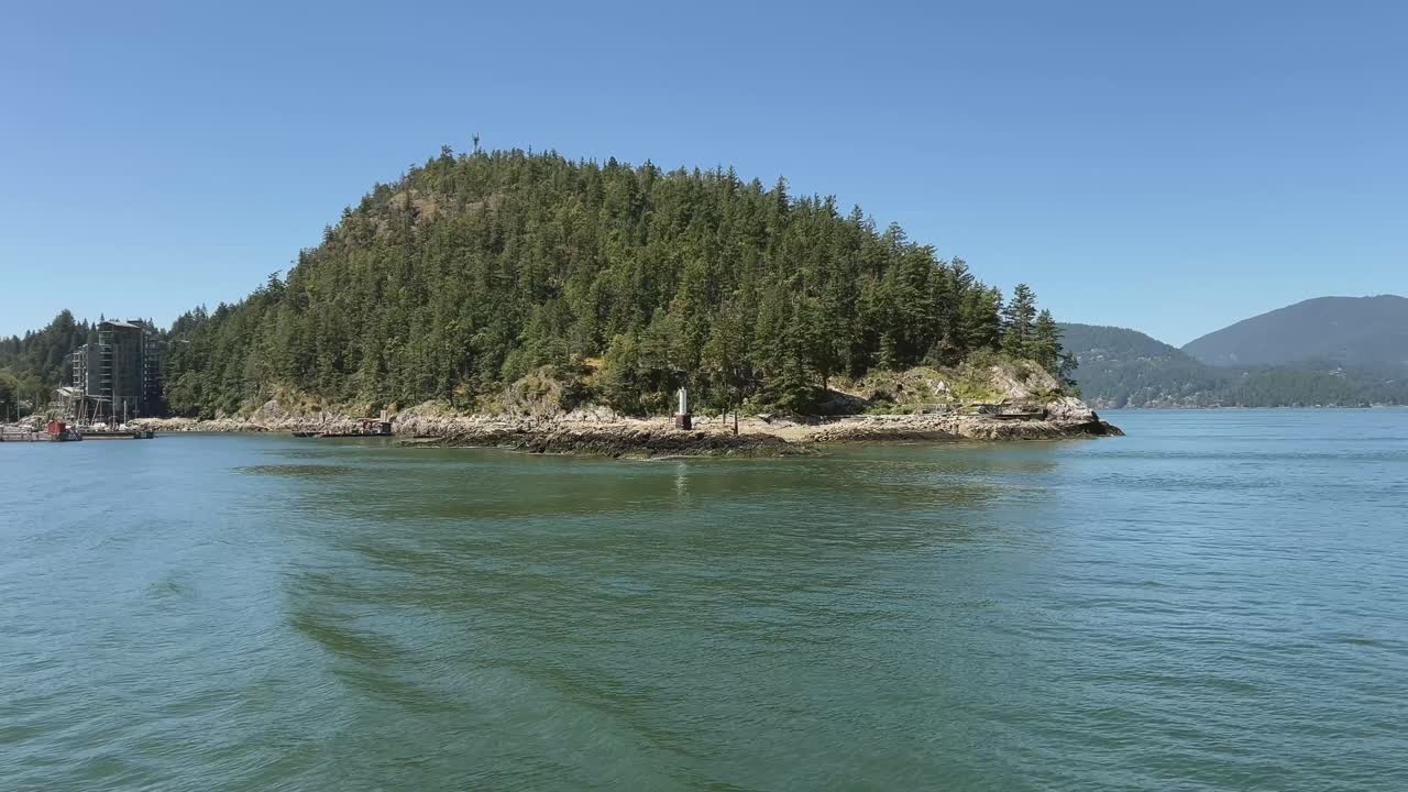 View from ferry departing Horseshoe Bay, passing rocky shoreline and forested hillside on a clear summer day in coastal British Columbia
