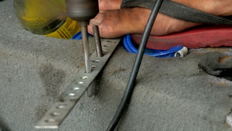 Close-up-of-a-mechanic-drilling-holes-on-a-piece-of-metal,-using-an-electric-hand-drill