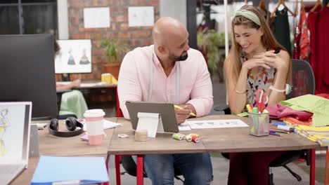 Happy-diverse-female-and-male-designer-discussing-designs-at-fashion-studio,-in-slow-motion