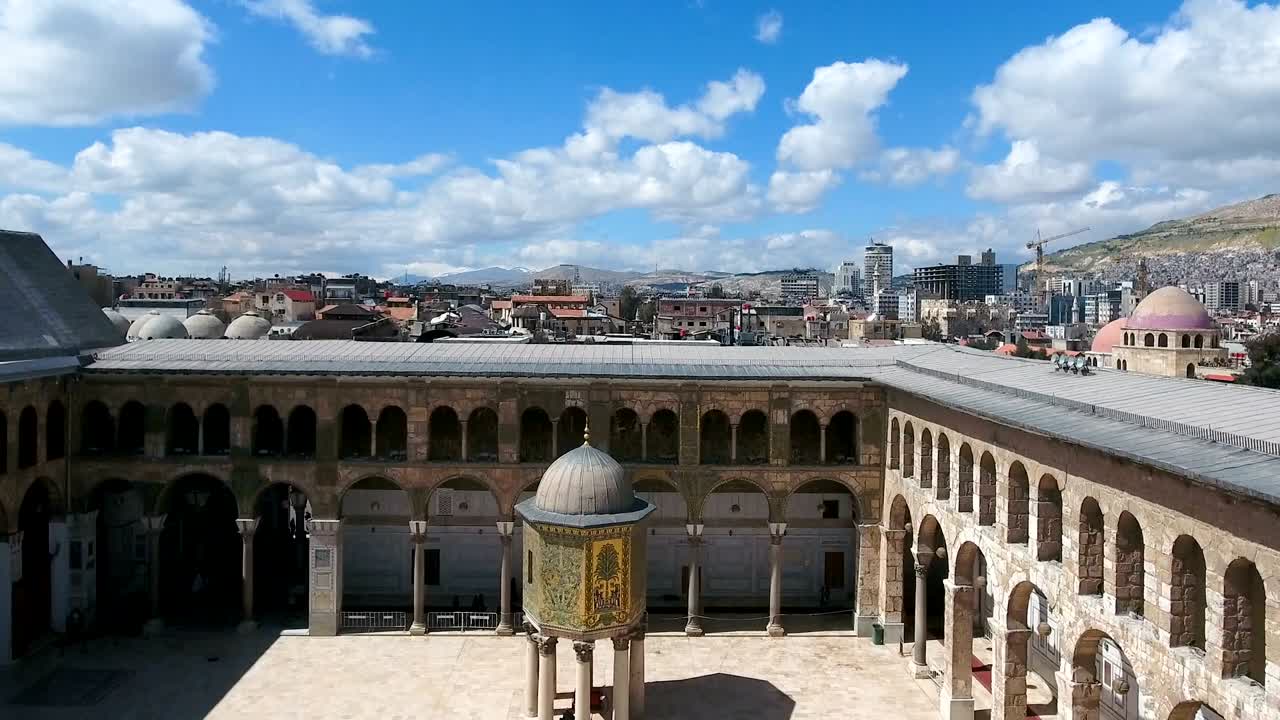 una vista aérea del centro de la mezquita de los umayyad en siria. un avión no tripulado está volando en el patio interior de la mesquita, donde vemos el exterior del edificio dentro de la mezquina.