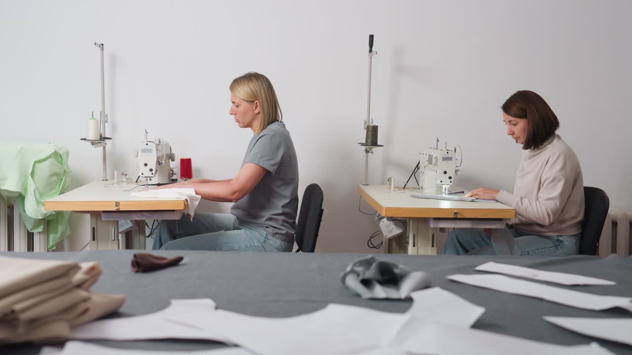 Round view of seamstress sewing material, table with fabrics on top, demonstrating collaborative garment production, showcasing minimal workspace, posture, method, and careful skill