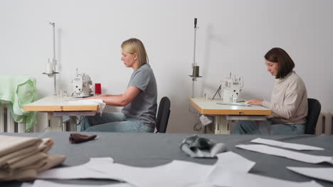 round view of seamstress sewing material, table with fabrics on top, demonstrating collaborative garment production, showcasing minimal workspace, posture, method, and careful skill