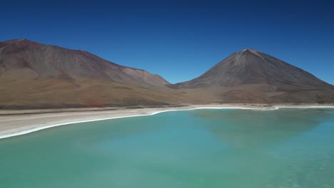 aerial drone shot flying high over large turquoise colored lake water surrounded by mountain range in bolivia on a sunny day