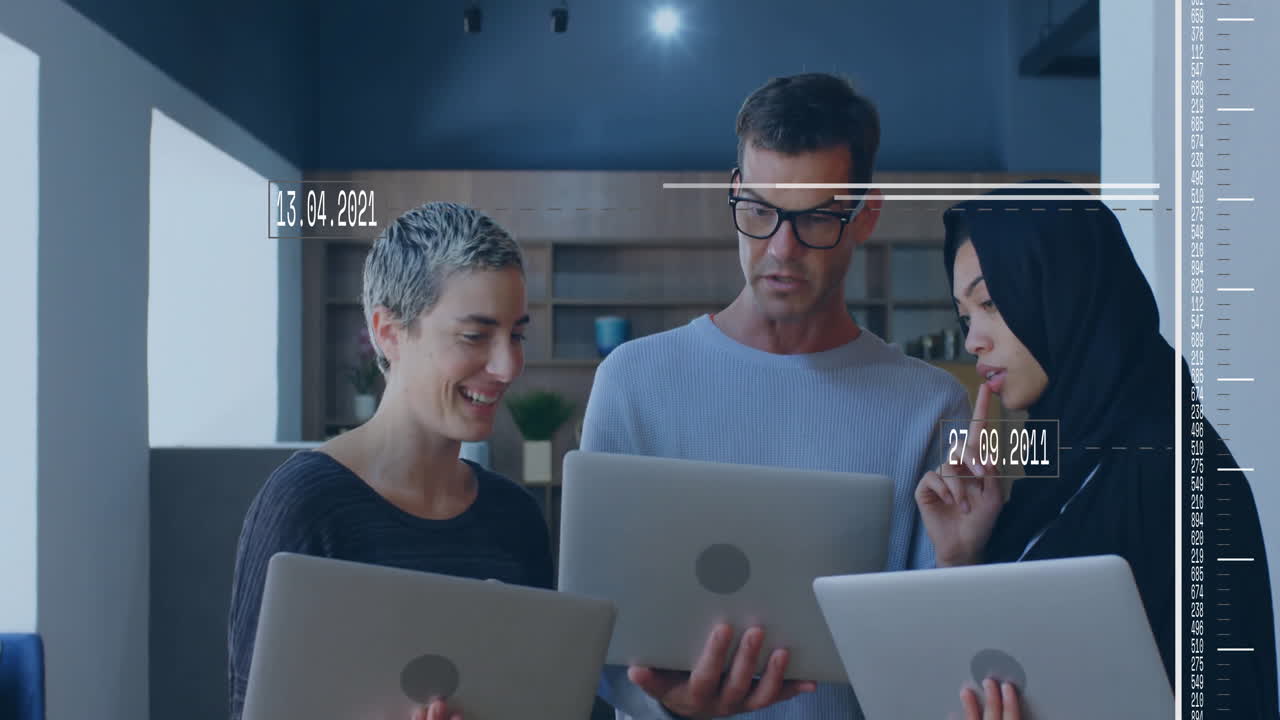 Three colleagues standing in office, reviewing business data on laptops, showing date overlays