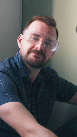 handsome bearded man in blue checkered shirt dances sitting near switch on light green wall at construction in modern room