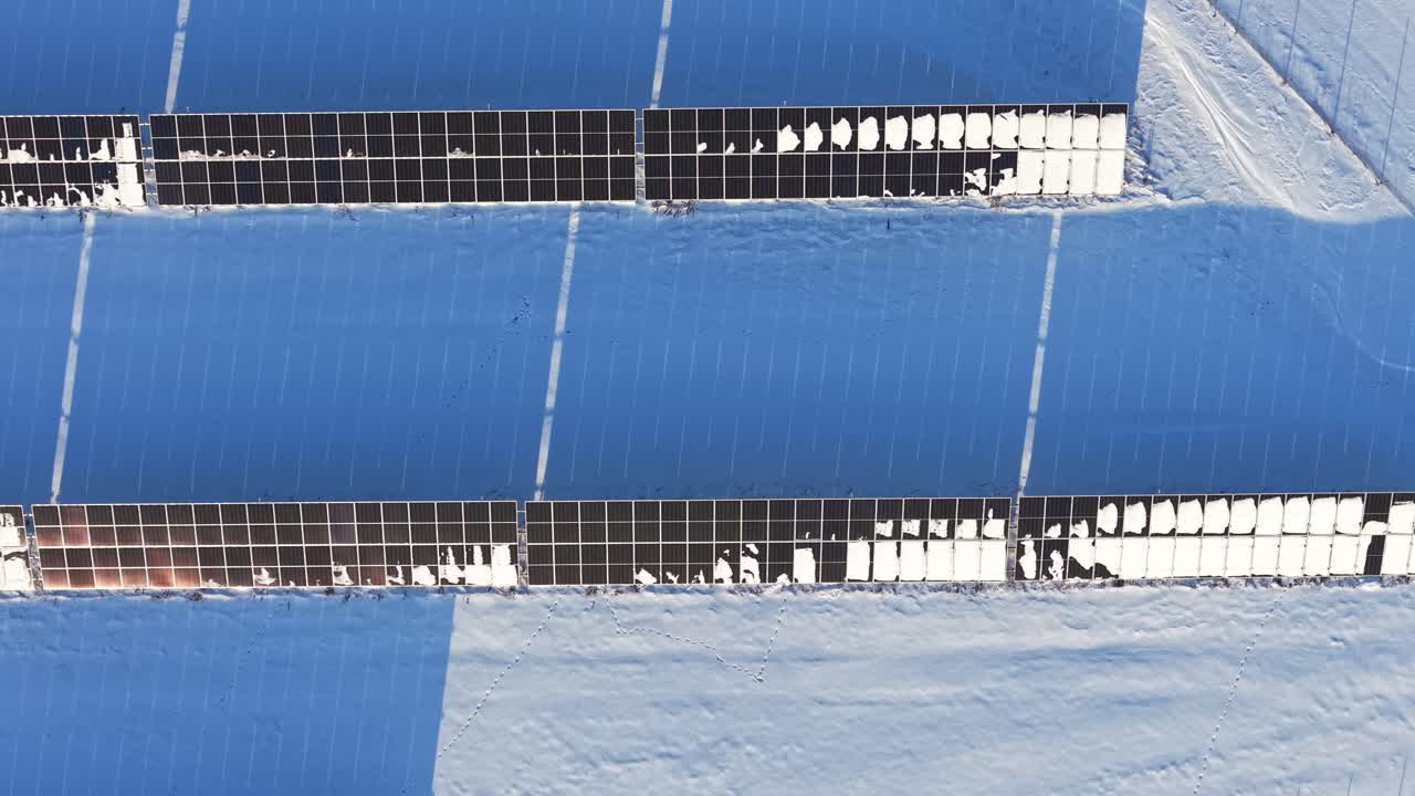 Řady sněhem pokrytých solárních panelů zdůrazňující obnovitelnou energii během zimy, letecký záběr shora s panoramatickým pohledem na texturu.