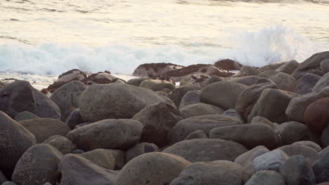 Closeup-shot-of-waves-hitting-the-rocks-by-the-coast-with-a-flock-of-birds-resting-among-the-rocks-in-San-Bartolo,-Lima,-Peru