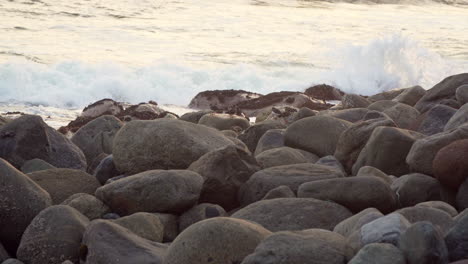 closeup shot of waves hitting the rocks by the coast with a flock of birds resting among the rocks in san bartolo, lima, peru