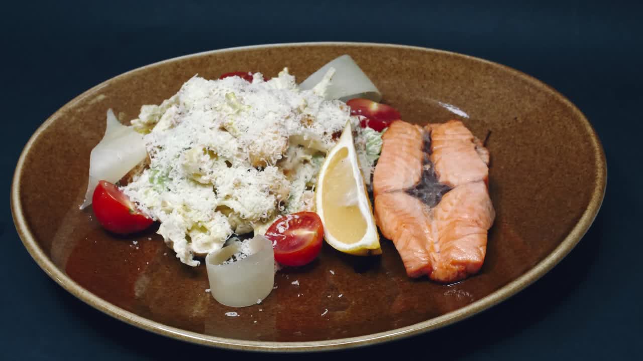 pescado rojo frito y lechuga salpicada de parmesán con una rebanada de limón en un plato sobre un fondo negro en resolución 4k