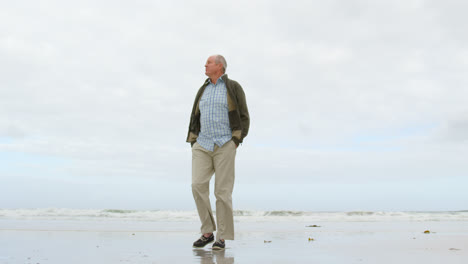 low angle view of old caucasian senior man walking with hands in pocket at beach 4k