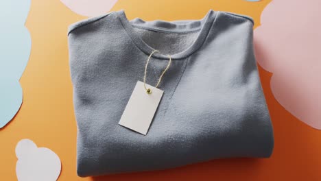 video of close up of blue folded t shirt with tag on orange background