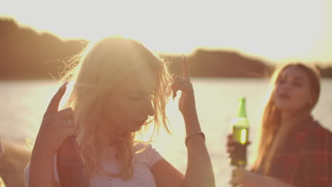 Una-Joven-Rubia-Caliente-Mueve-Maravillosamente-Sus-Manos-Bailando-En-La-Fiesta-Caliente-En-La-Playa-Con-Cerveza.-Este-Es-Un-Feliz-Verano-En-La-Fiesta-Al-Aire-Libre-En-La-Playa-De-Arena-Cerca-Del-Lago.