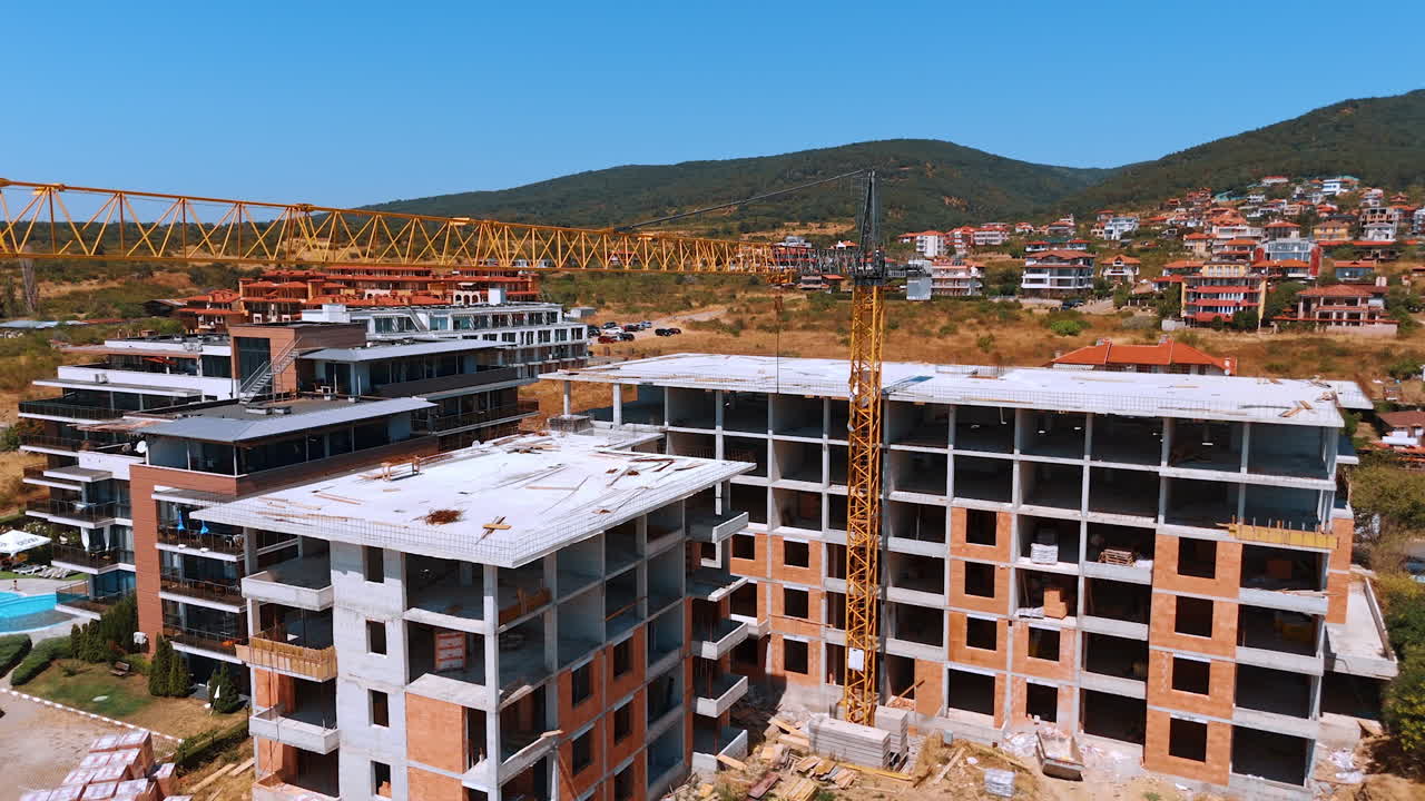 New apartment complex rising. A large residential complex is being built with cranes and construction materials under a clear blue sky