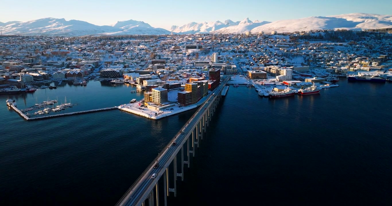 Vue aérienne du port de Tromsø, Norvège, avec un front de mer moderne, une marina et un long pont, par une calme journée d'hiver ensoleillée en Europe du Nord.