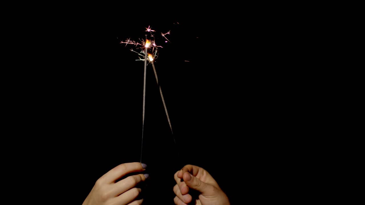Close-up of hands holding and waving bengal fire burning sparklers in front of black background