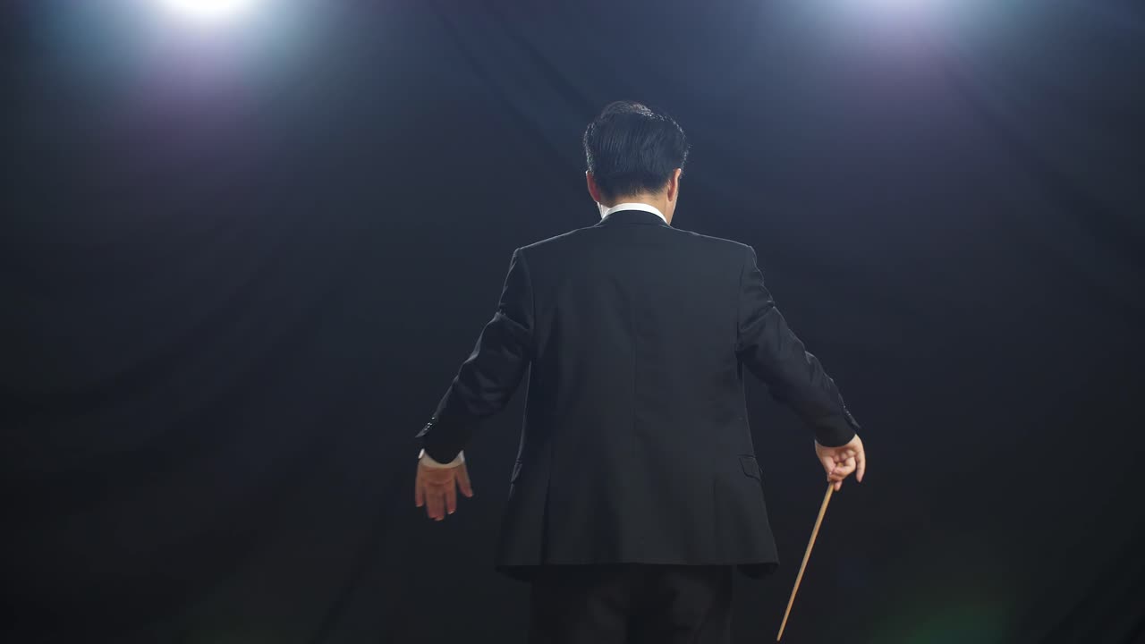 Back View Of Asian Conductor Man Holding A Baton And Showing Gesture In The Black Studio
