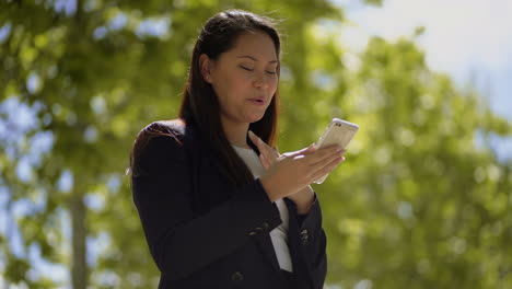 Mujer-Joven-Sonriente-Usando-Un-Teléfono-Inteligente-Al-Aire-Libre