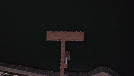 Drone-top-down-ascend-above-T-shaped-wooden-dock-pier-with-fishermen-along-boardwalk-with-homes