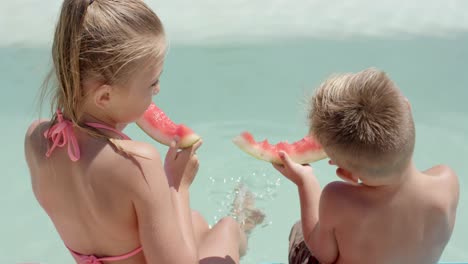 happy caucasian siblings eating watermelon at swimming pool at beach house