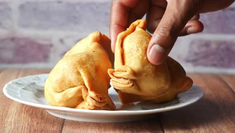 close-up of a hand picking up a samosa from a plate