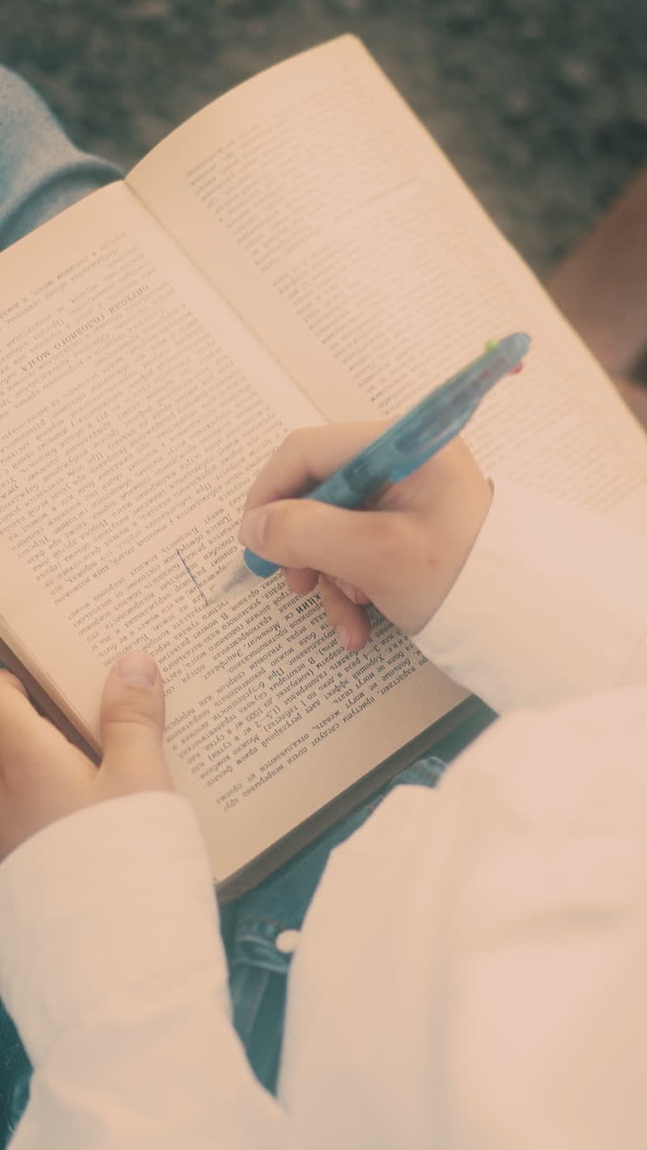 young guy in white shirt and blue jeans draws on textbook sheet with blue pen extreme close vertical view