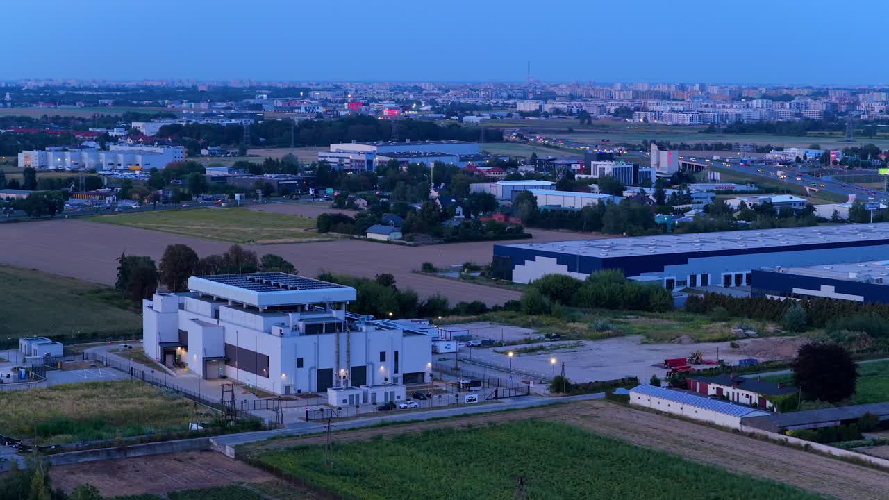Aerial view of modern data center building and logistics warehouse in background. Suburb district of Warsaw at dusk. Traffic on highway in Poland. Wide shot