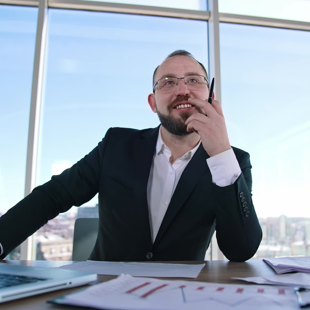Um empreendedor sorrindo no escritório. Retrato de um empresário de óculos sentado à mesa com um laptop. Funcionário de escritório em um ambiente interno.