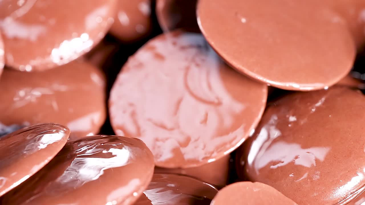A detailed look at shiny chocolate discs stacked closely together, highlighting their smooth texture and glossy finish.