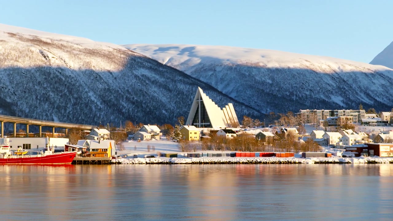 Bateau rouge et église blanche emblématique entourés de montagnes enneigées à Tromsø, Norvège. Vue latérale par drone aérien, vol à basse altitude