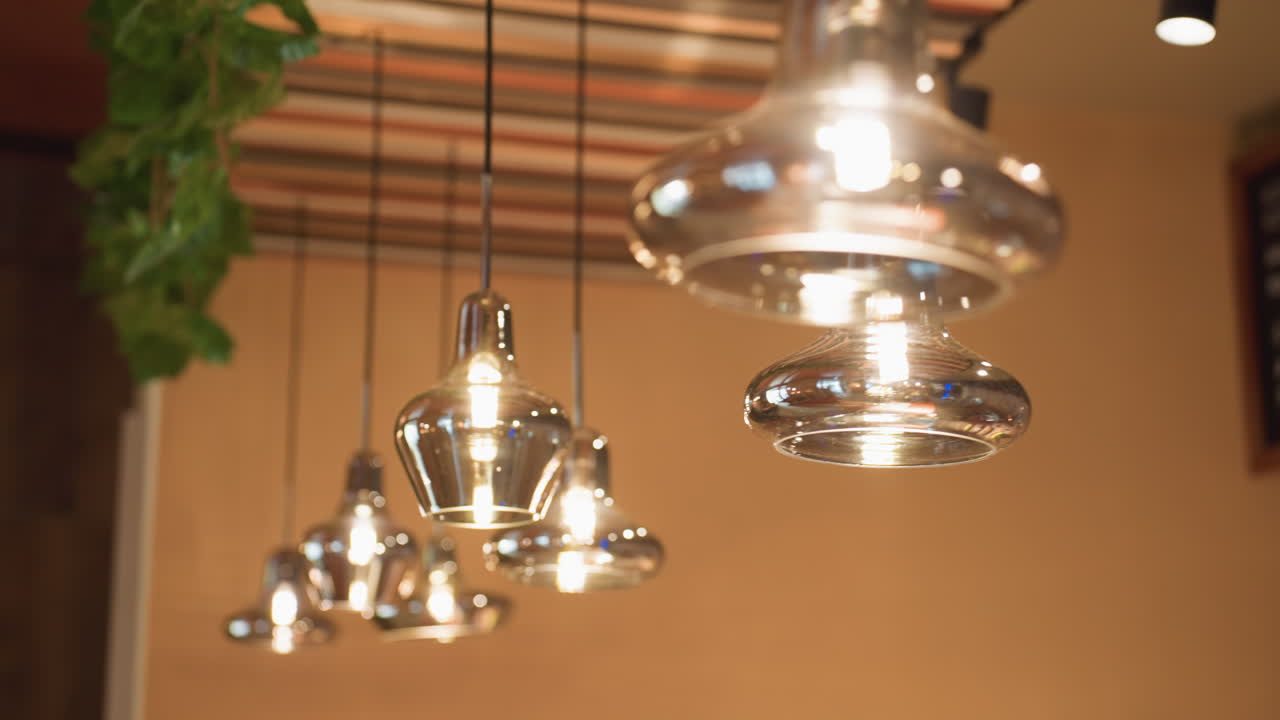 Close up of glowing glass pendant lights suspended from striped ceiling in stylish bar interior, soft focus in background with lush green ivy enhancing warm cozy ambiance