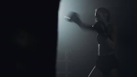 woman shadow boxing in a dark gym with dramatic lighting